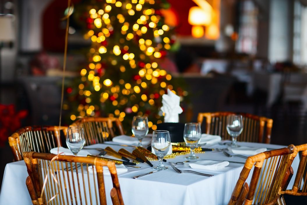 Festive holiday table setting in a restaurant with Christmas tree lights in the background.